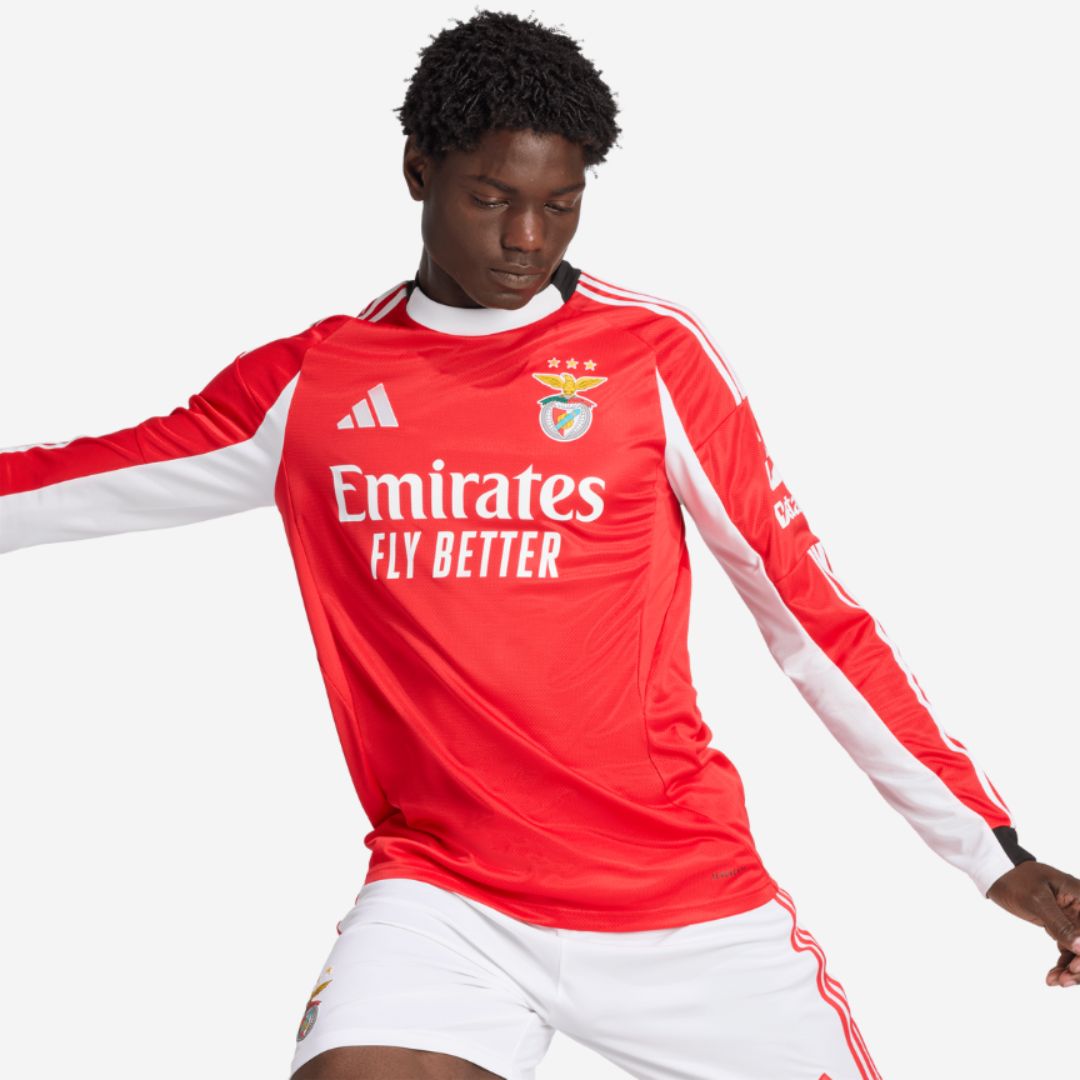 Camisa Benfica home 25/26 manga longa na cor vermelha com destaque para o logo Emirates e ícones do clube.