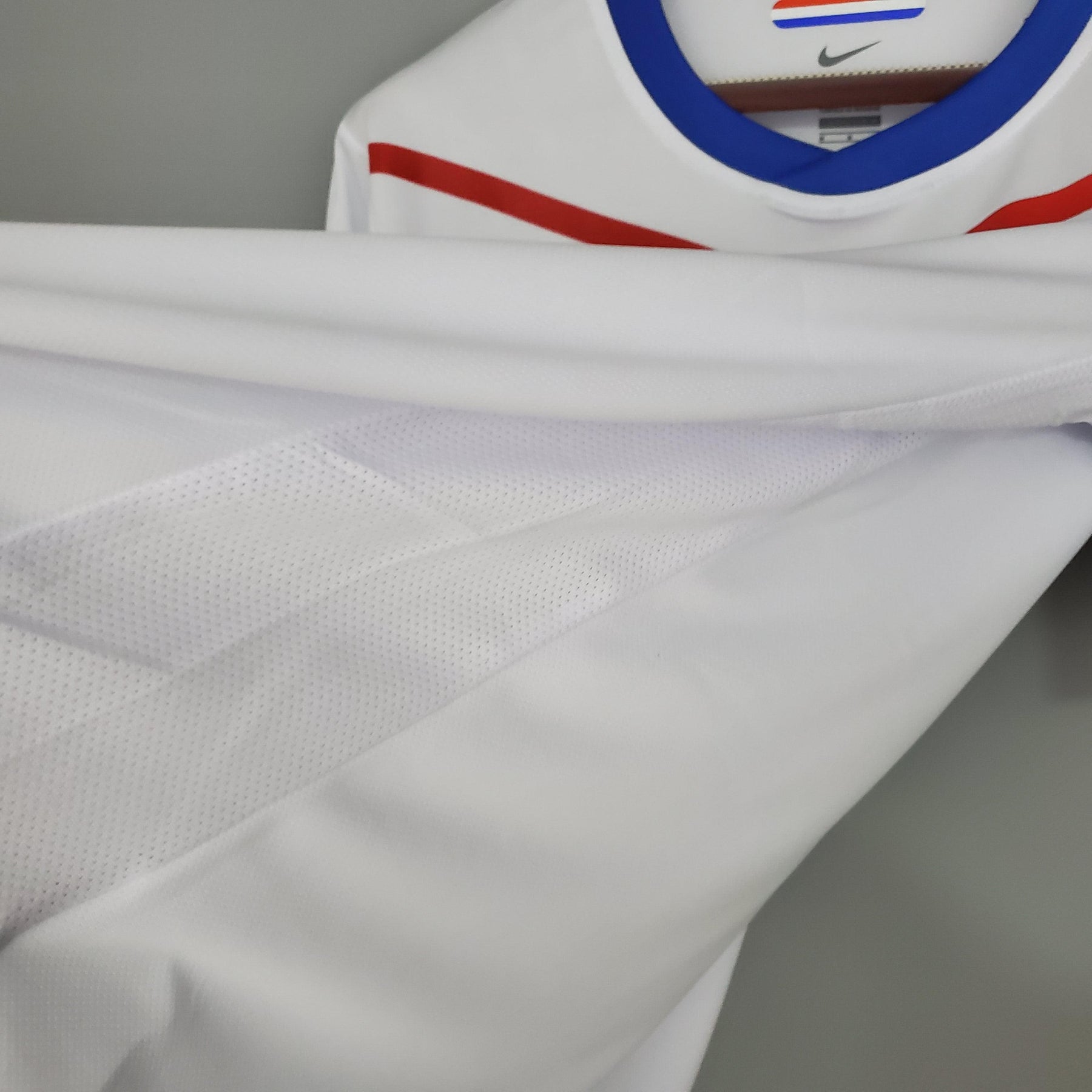 Camisola Holanda Away 12/13 Retro em detalhe, tecido branco com listras vermelhas e azul, disponível na OLYMPIC STORE.
