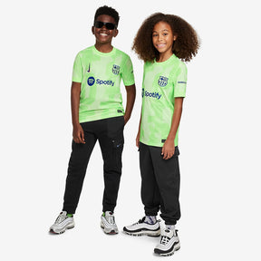 Conjunto Infantil Nike FC Barcelona 2024/25 III com camiseta verde e calças pretas, crianças felizes posando.