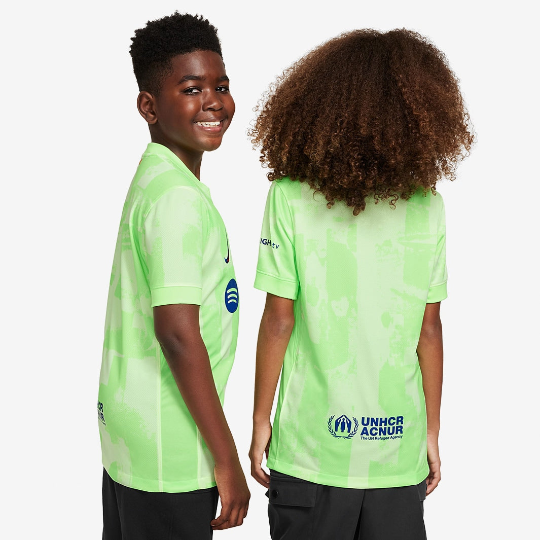 Conjunto Infantil Nike FC Barcelona 2024/25 III, meninos usando camisa verde com detalhes ao fundo.