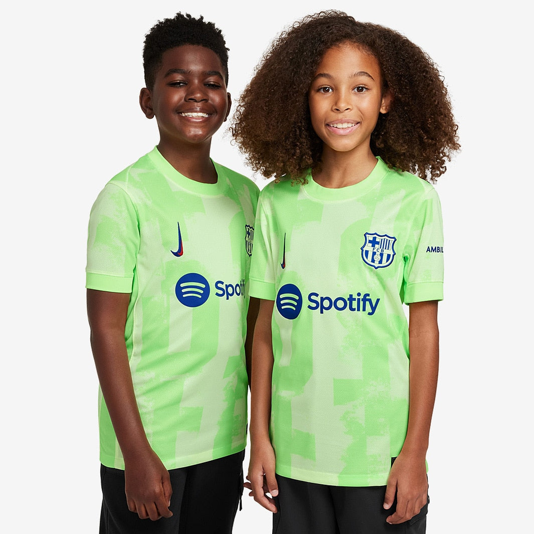 Conjunto Infantil Nike FC Barcelona 2024/25 III em destaque com duas crianças vestindo camisetas verdes.