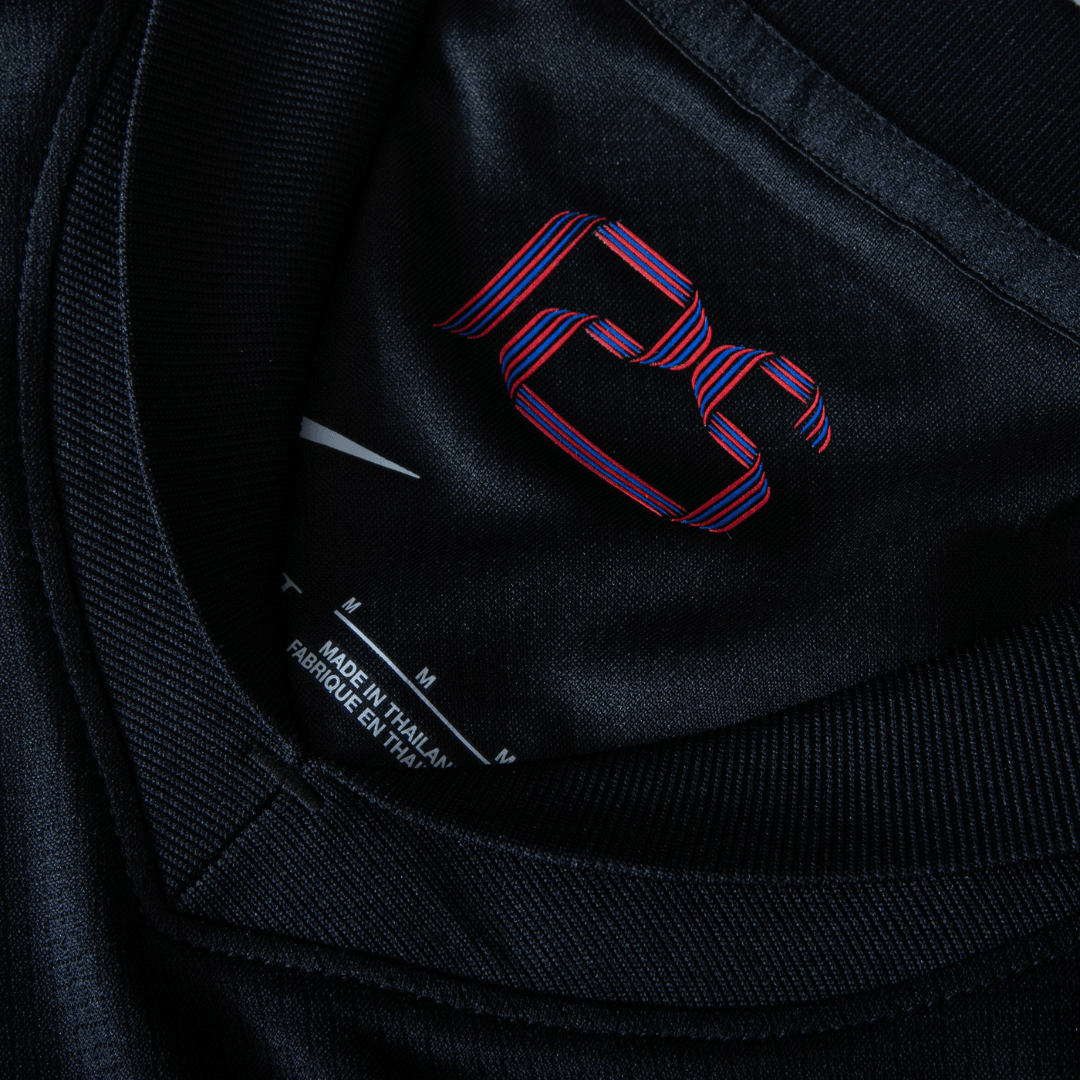Detalhe da etiqueta interna da camisola Barcelona away 24/25 com o logotipo em vermelho e azul.