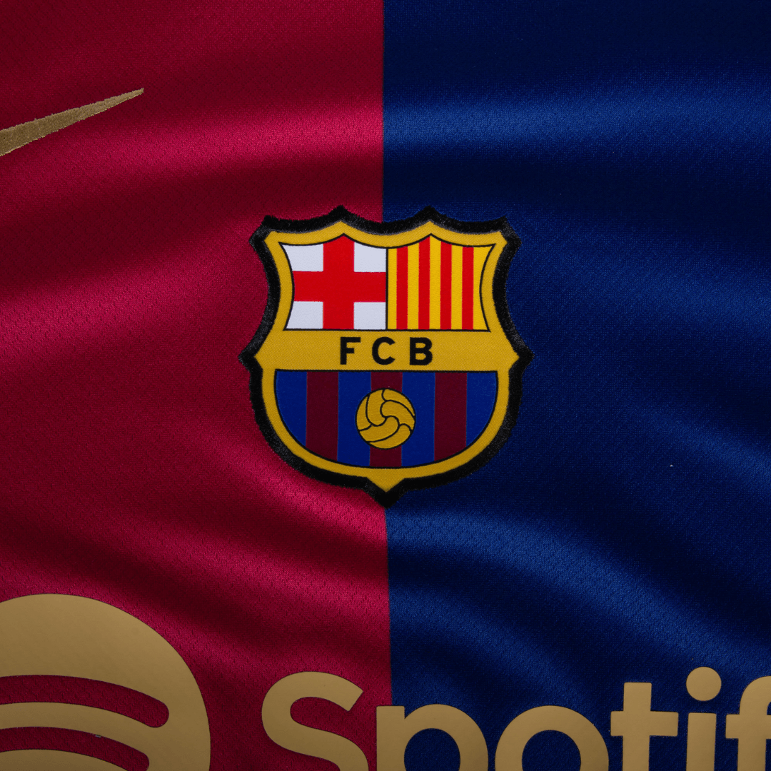 Emblema do Barcelona home 24/25 em camisa, com cores azul e grená. Barcelona home, produto oficial do clube.