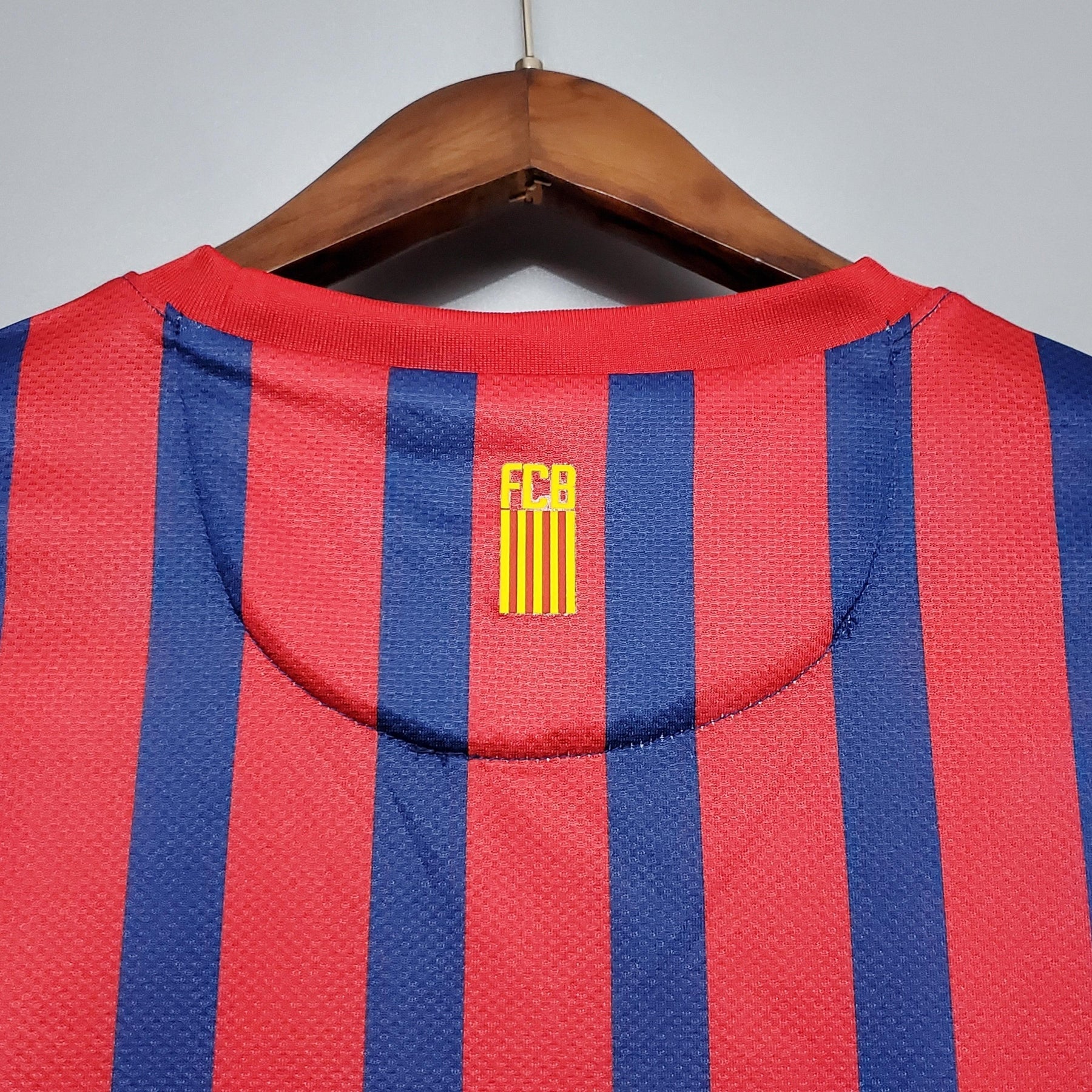 Camisa Barcelona Home 11/12 Retro com detalhes em azul e vermelho, mostrando o emblema FCB.