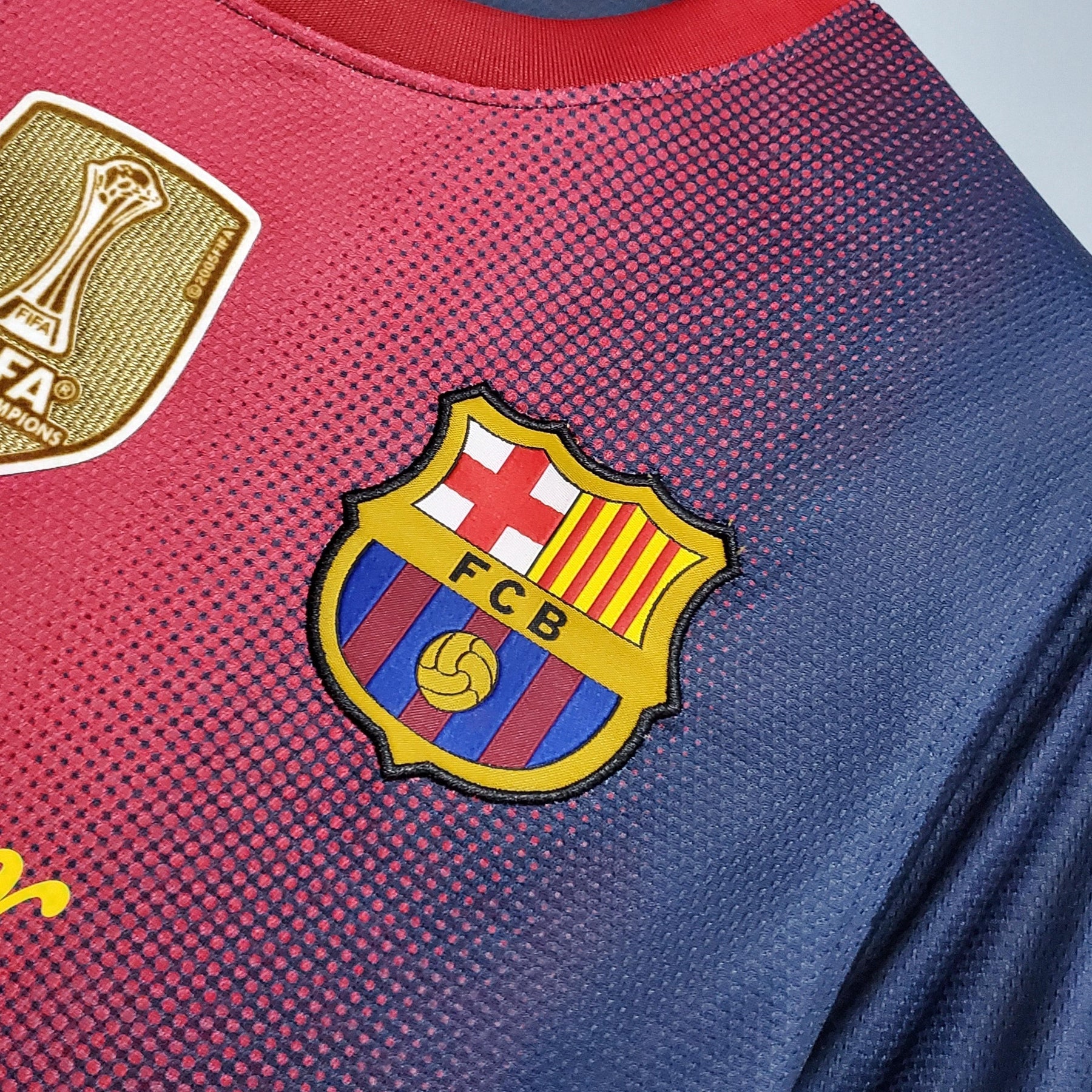 Banda da camisa Barcelona Home 12/13 Retro com o icônico escudo do Barcelona e detalhes da FIFA.