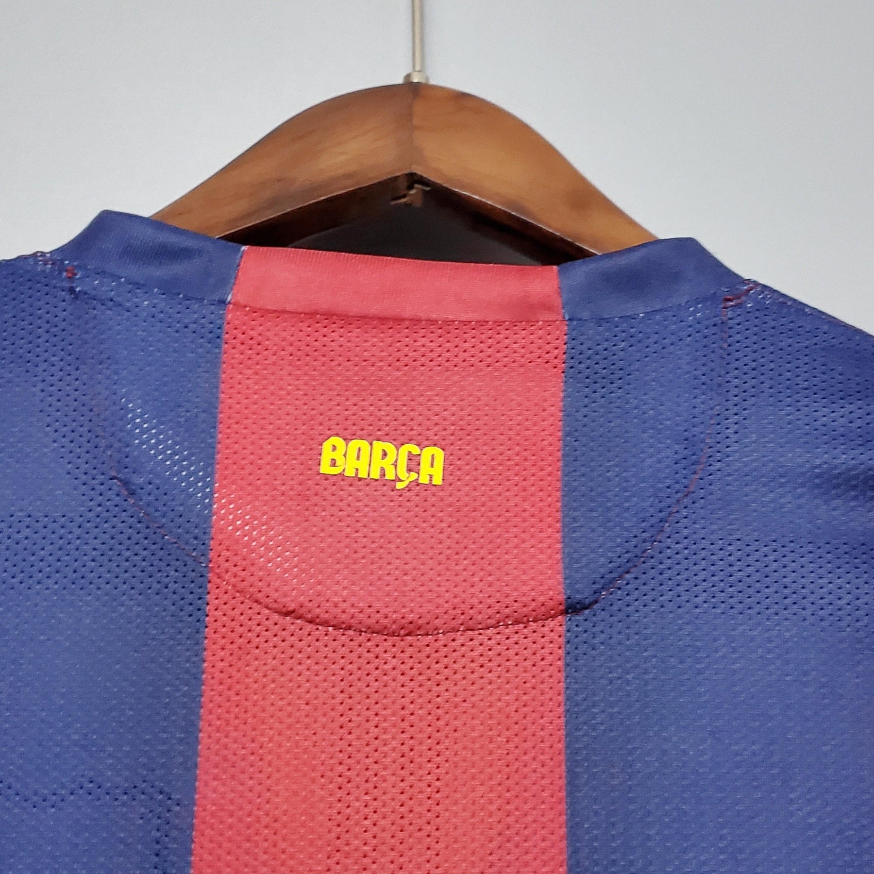 Camisa do Barcelona com detalhe em amarelo nas costas, mostrando a palavra BARÇA na parte de trás.