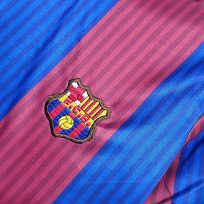 Emblema do FC Barcelona em camisa listrada das cores azul e grená, representando o Barcelona.