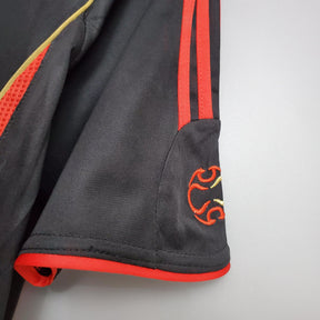 Detalhe da manga do uniforme AC Milan 2006 Retro Black Olympic com detalhes em vermelho e dourado.