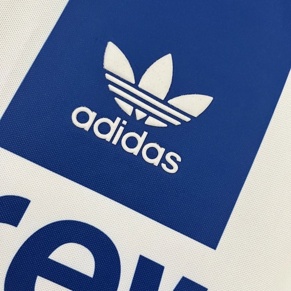Logotipo da Adidas em camisola retro azul e branca, representando a clássica marca esportiva.