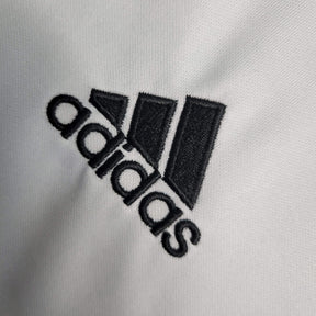 Logo da marca adidas em destaque, bordado em preto sobre tecido claro.