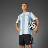 Jogador vestindo a camisola Argentina home 24/25 - Comemorativa, segurando uma bola de futebol.