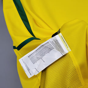 Camisola Brasil Home 2002 Retro com detalhes em amarelo e etiqueta de cuidados visível.