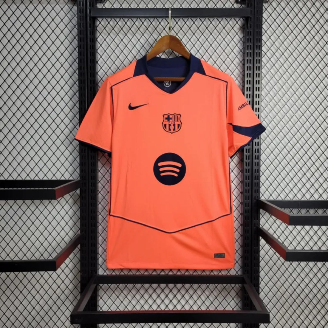 Camisola FC Barcelona third laranja 2025/26 - TOTAL 90 exposta em exibição com detalhes da marca Nike e logo do Spotify.