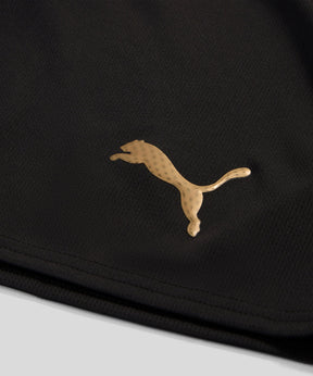 Detalhe do logo dourado da marca Puma em uma camisola preta.