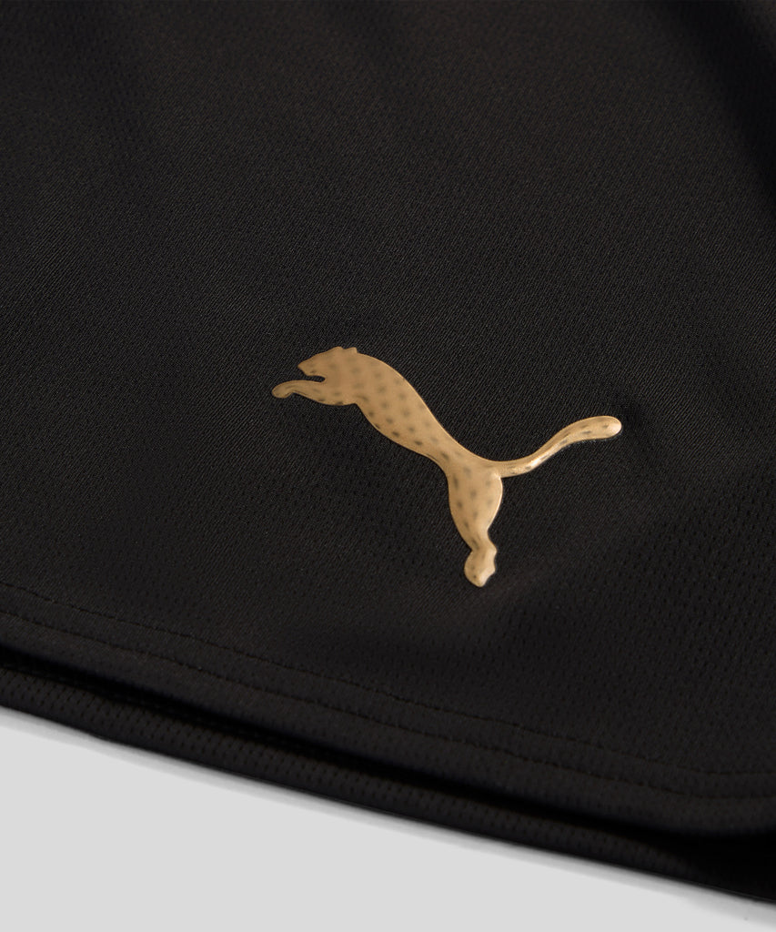 Detalhe do logo dourado da marca Puma em uma camisola preta.