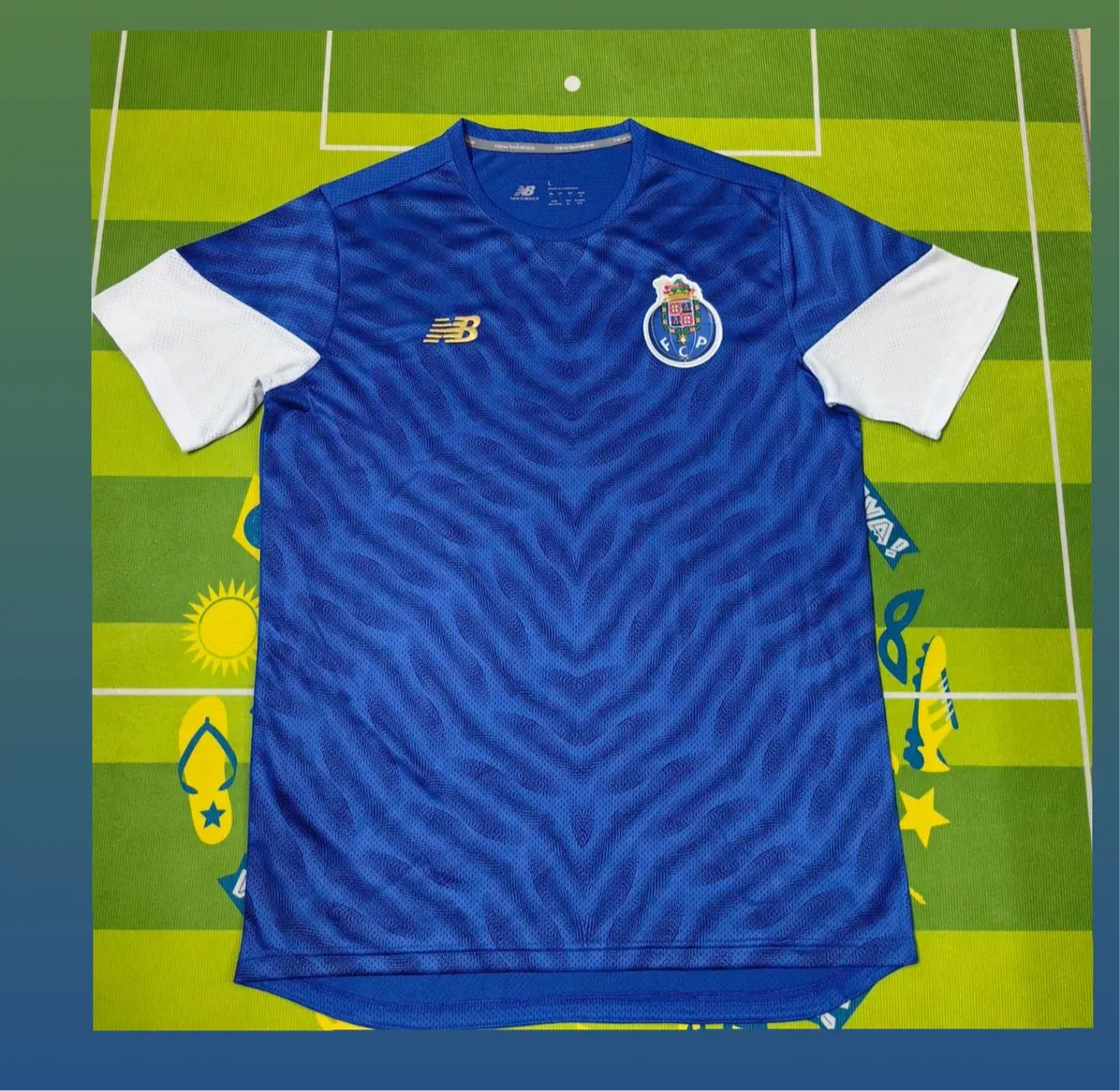 Camisola PRÉ JOGO FC Porto azul 2025/26 com símbolo bordado em fundo verde de campo de futebol.