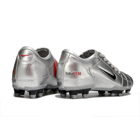 Chuteira Nike Total 90 FG Prateada com design prateado e detalhes em vermelho, ideal para campos naturais.