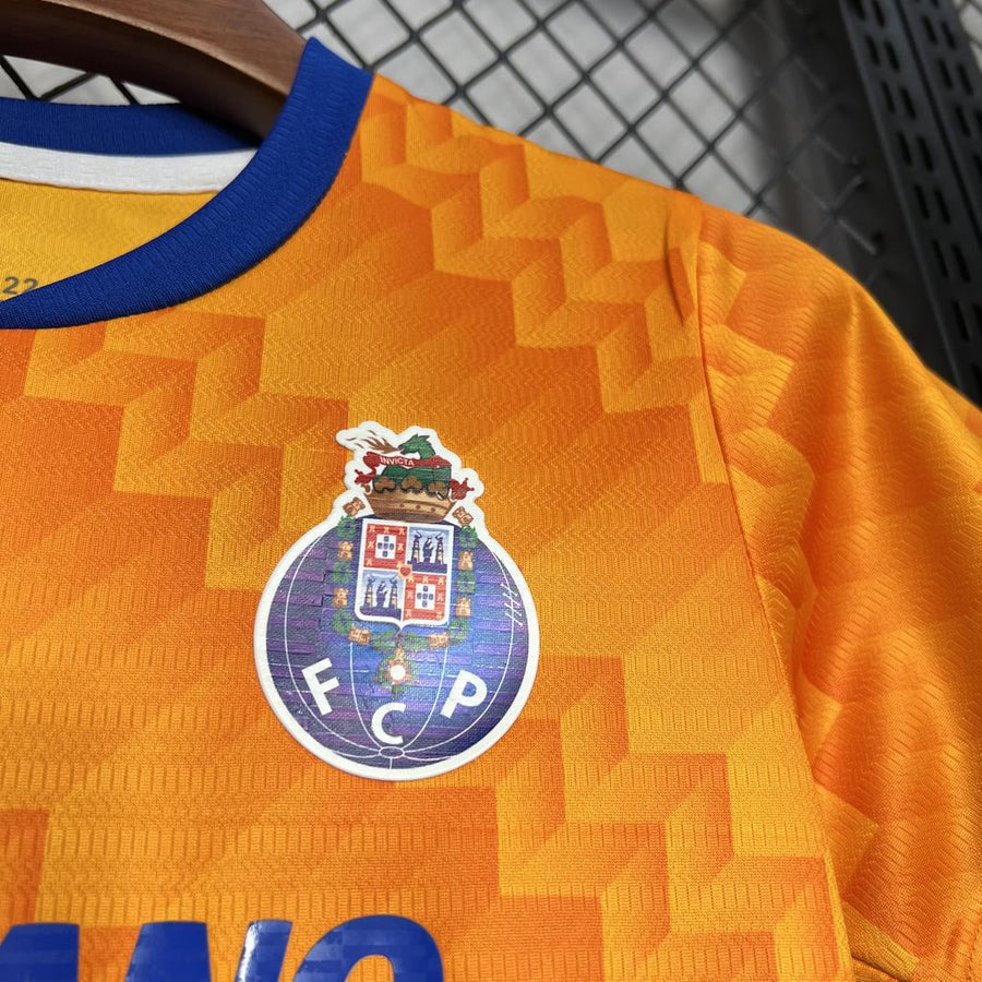 Conjunto infantil FC Porto laranja alternativo 2024/25 com logo em destaque na camisola.