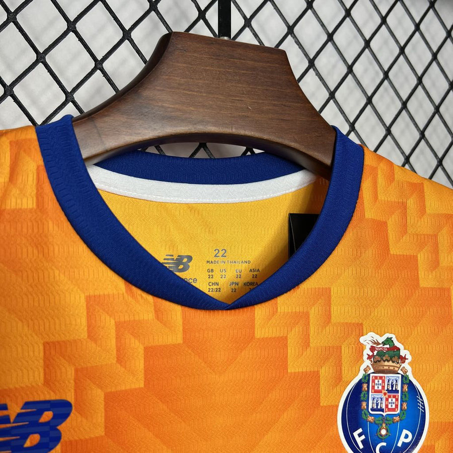 Conjunto infantil FC Porto laranja alternativo 2024/25 exposto em cabide, detalhe do acabamento e logo.