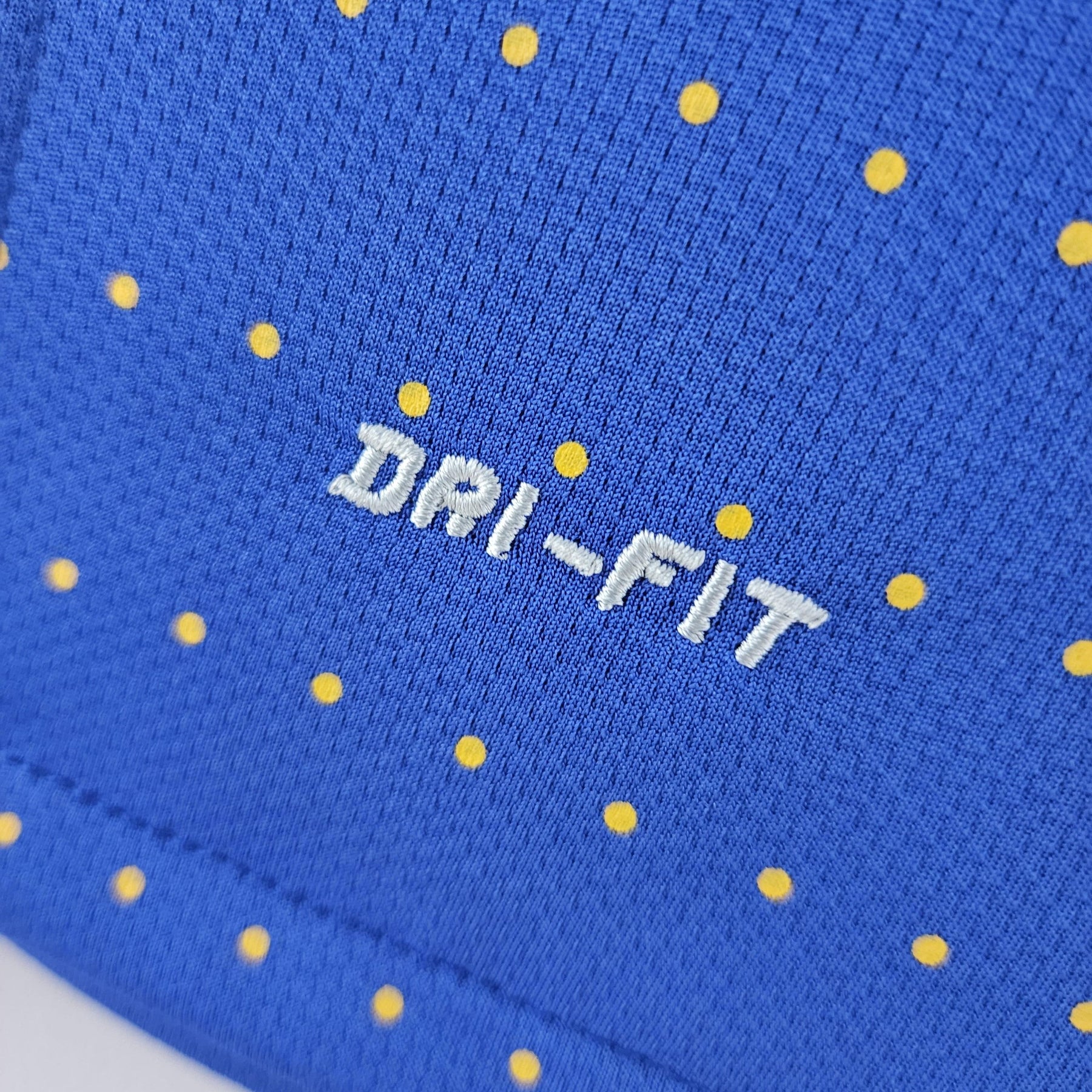 Detalhe da textura e estampa da camisola Brasil, destacando a tecnologia DRI-FIT em azul com bolinhas amarelas.