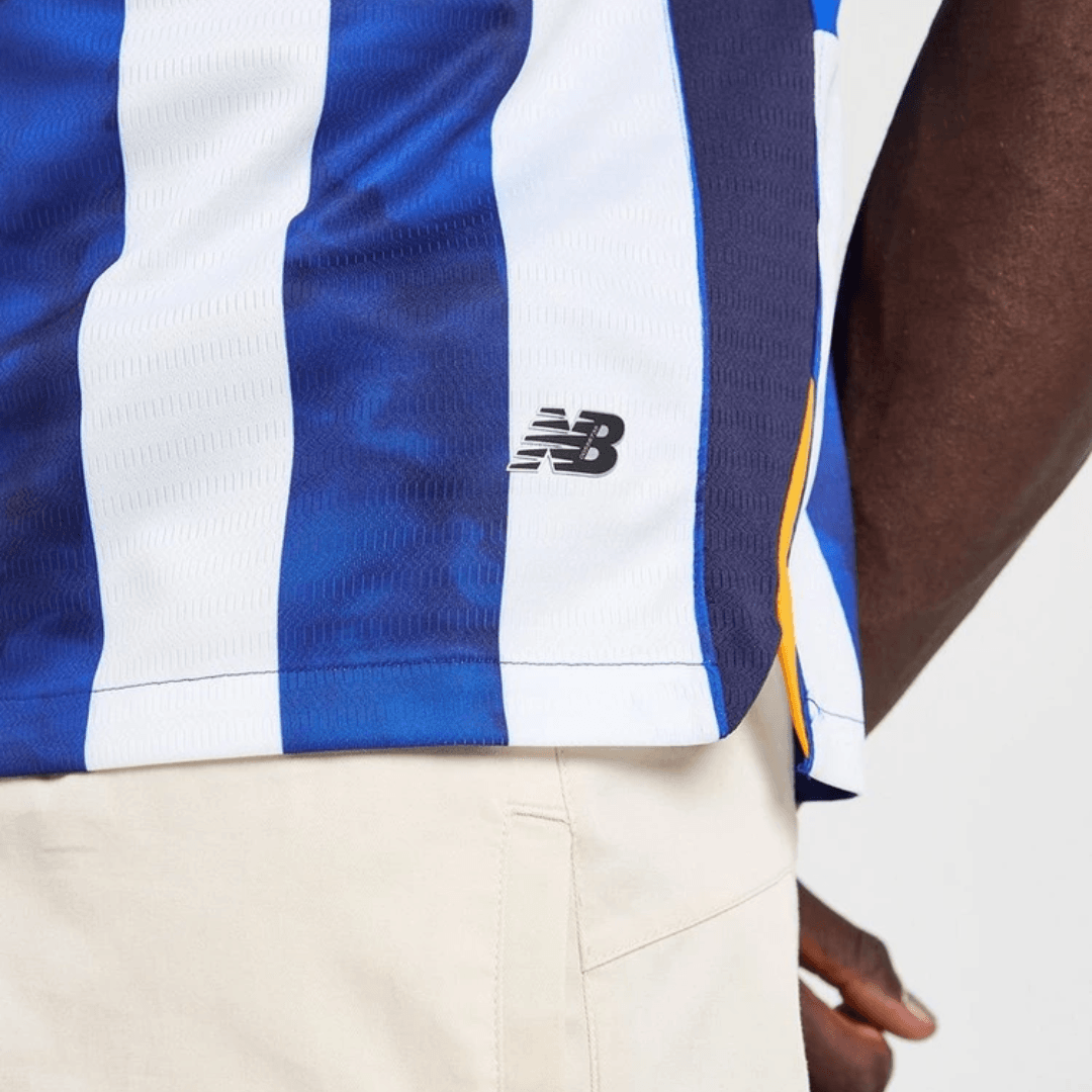 Camisa FC Porto 24/25 em azul e branco, detalhe da logomarca New Balance, vista lateral.