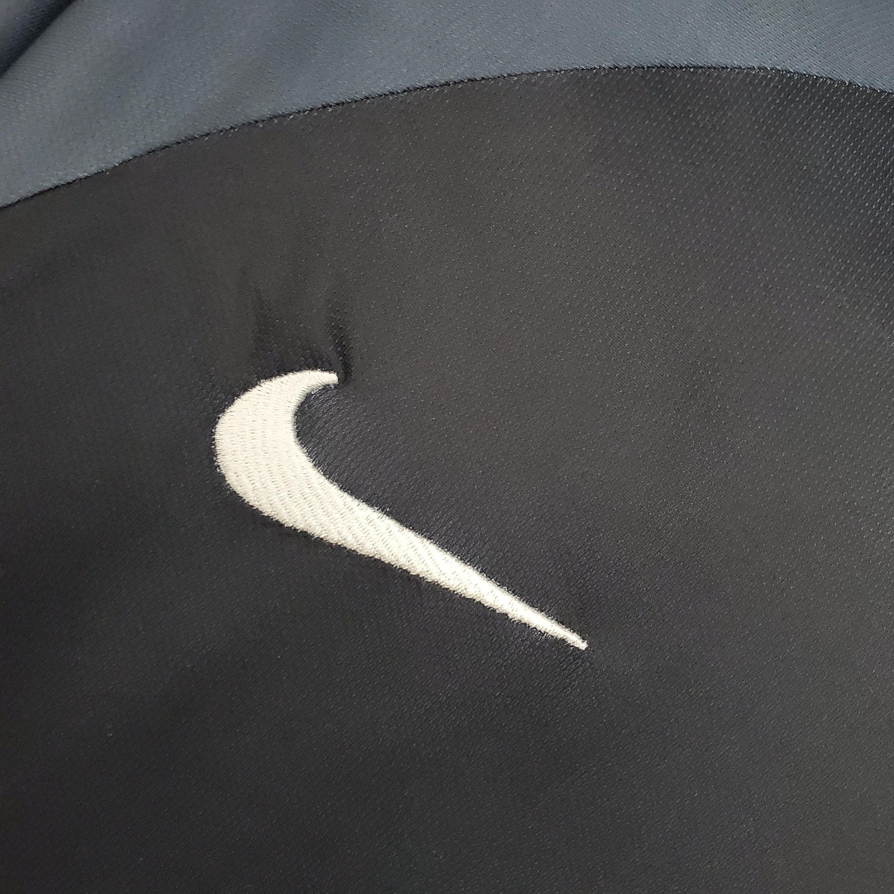 Logotipo da Nike em um tecido preto, parte de um produto PSG Away 01/02 Retro Azul Olympic.