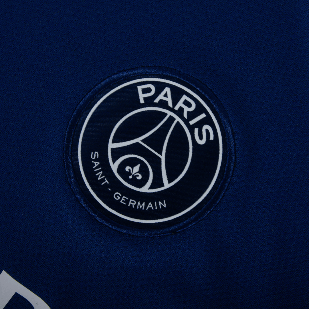 Logotipo do Paris Saint-Germain em camisola azul marinho da PSG fourth 24/25, destacando o emblema do time.