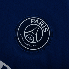 Logotipo do Paris Saint-Germain em camisola azul marinho da PSG fourth 24/25, destacando o emblema do time.