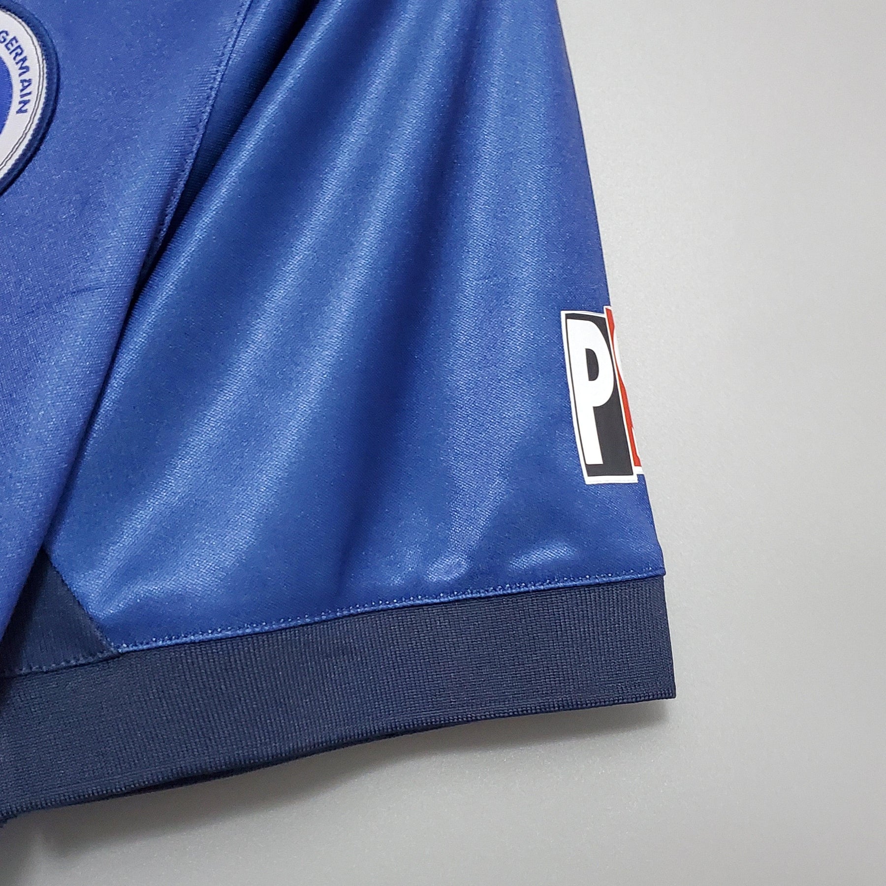 Detalhe da manga da camisola PSG Home 98/99 Retro Azul e Vermelho, mostrando textura e logo distintivo.